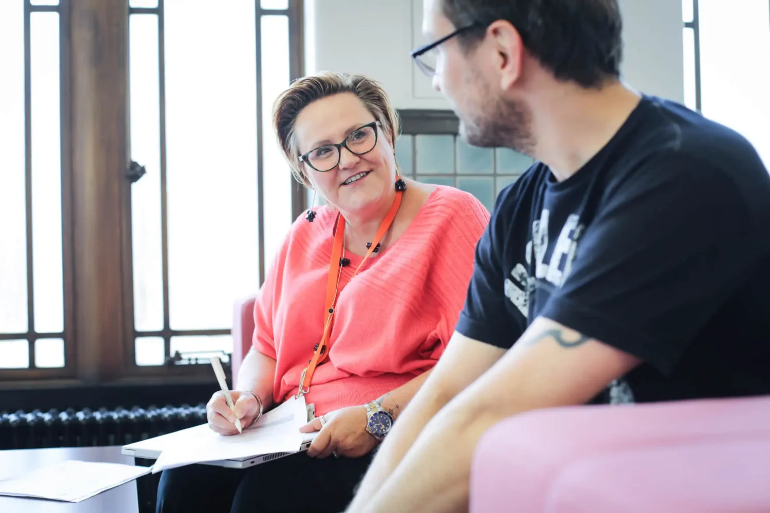 Person in peach blouse writing on a piece of paper while talking to younger person