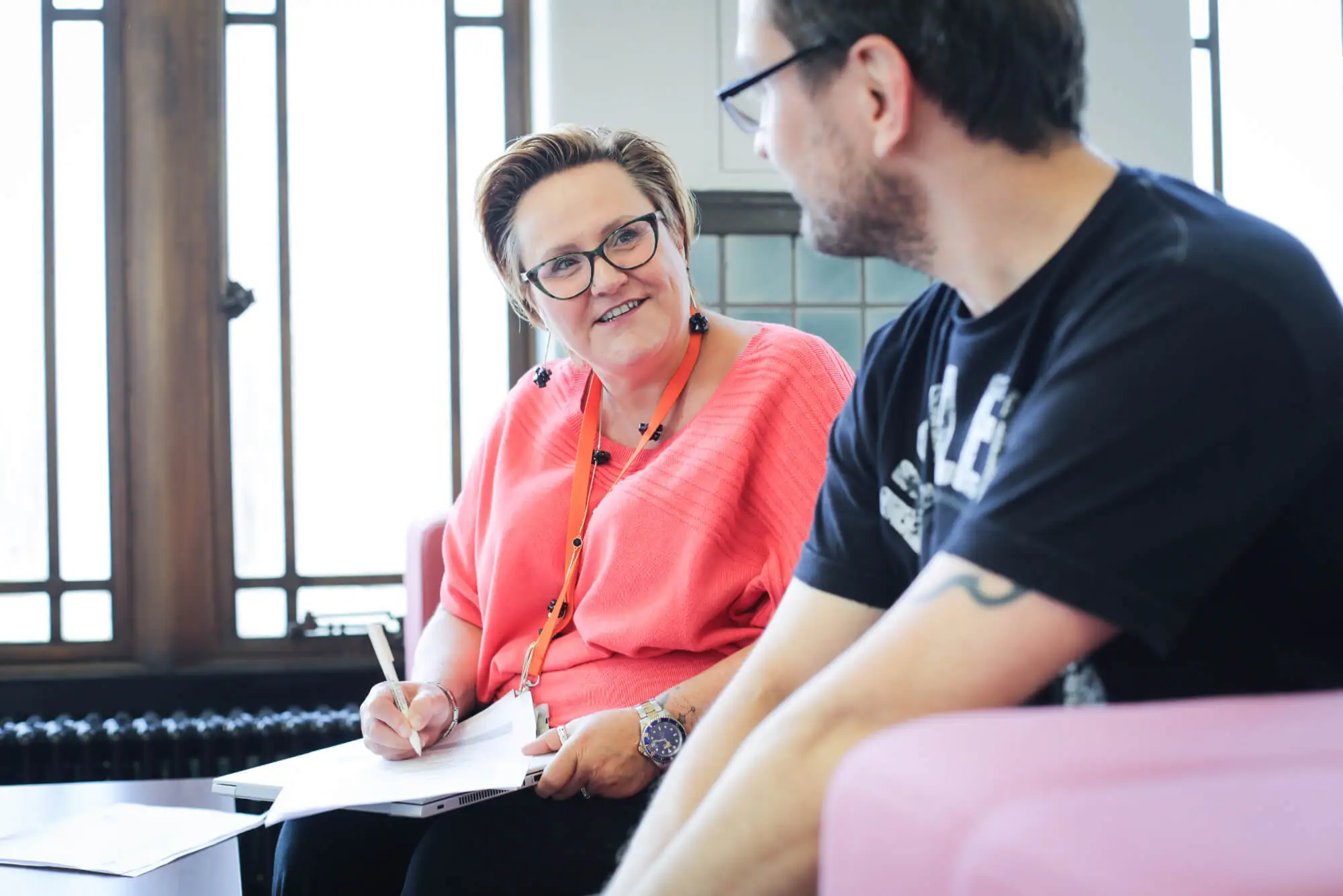 Person in peach blouse writing on a piece of paper while talking to younger person