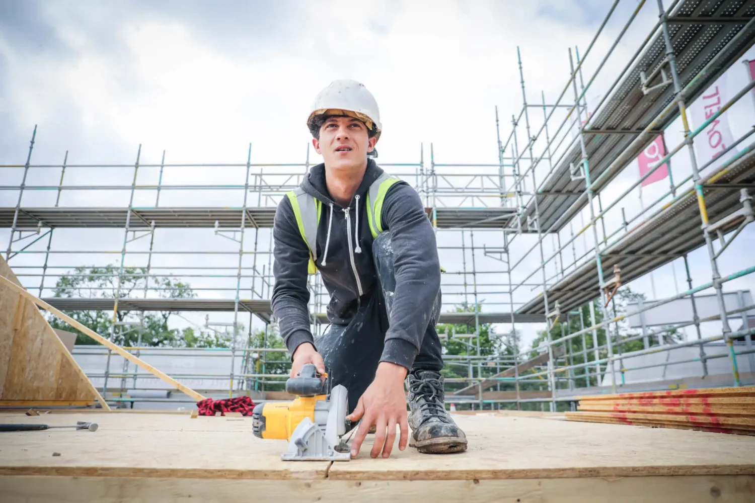 Person wearing hard hat looking up while kneeling down on construction site.