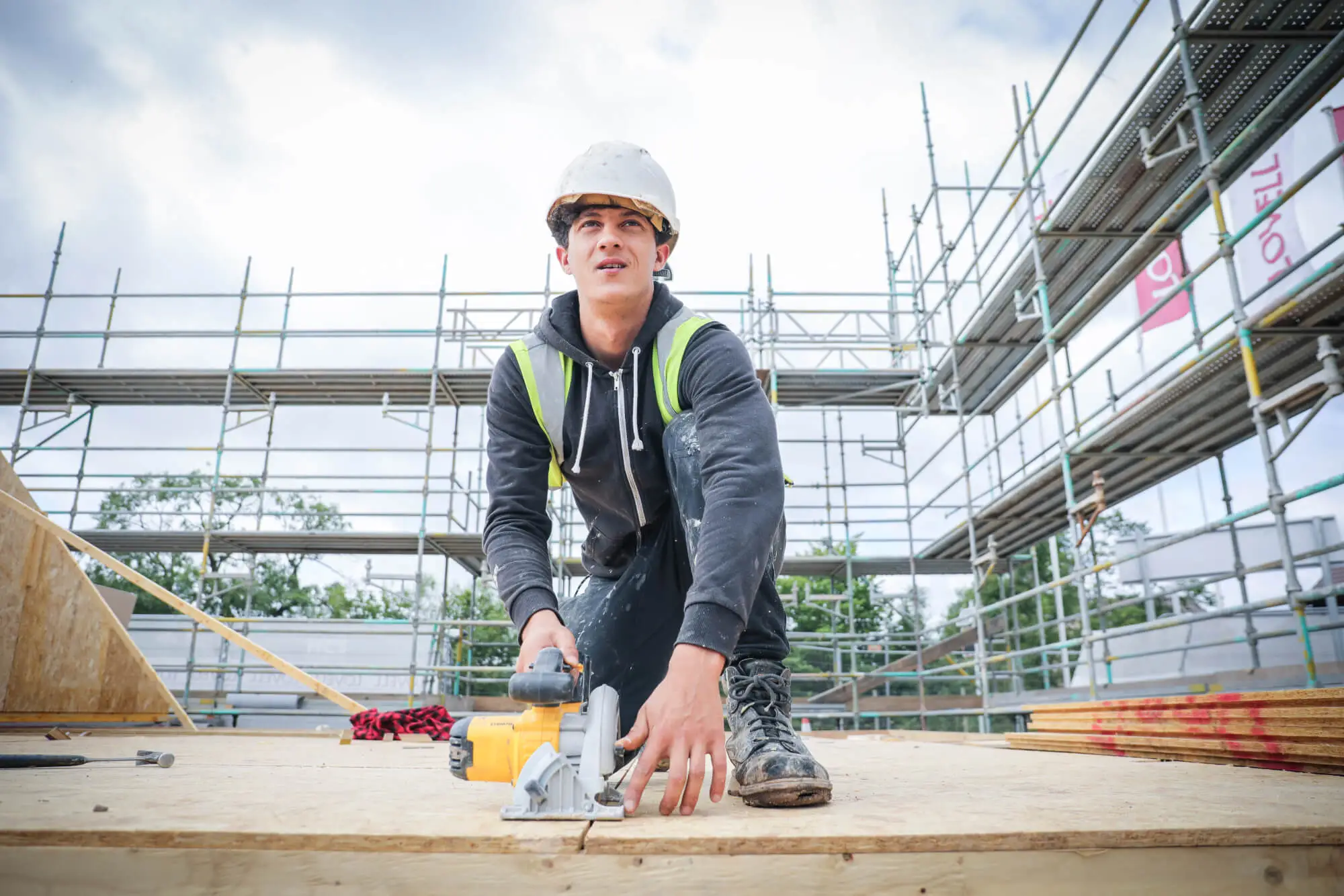 Person wearing hard hat looking up while kneeling down on construction site.